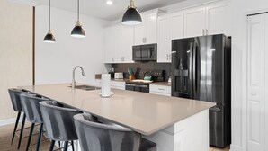 Une cuisine moderne dotée d’un îlot central, de meubles blancs, d’appareils électroménagers en acier inoxydable et de luminaires suspendus.