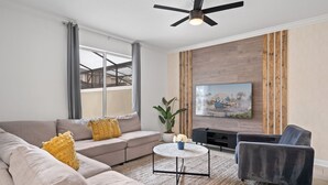 Un salon moderne comprenant un canapé, un fauteuil, une table basse et un téléviseur à écran plat fixé au mur.