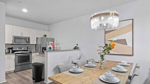 Eine moderne Küche mit Edelstahlgeräten, ein Essbereich mit einem Holztisch, gedeckt für vier Personen, und eine Chandelier.