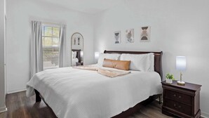 Ein Schlafzimmer mit einem großen Bett, Nachttischen, einer Nachttischlampe und Wandbildern.