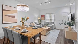 Ein modernes Wohnzimmer mit Esstisch, grauen Sofas, einem Kronleuchter und einem großen abstrakten Gemälde.