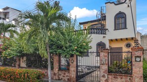 A two-story house with a stone gate, a palm tree, and a flower bed. - Casa Sandy - Private Golden Zone Villa with Pool (Bucerías)