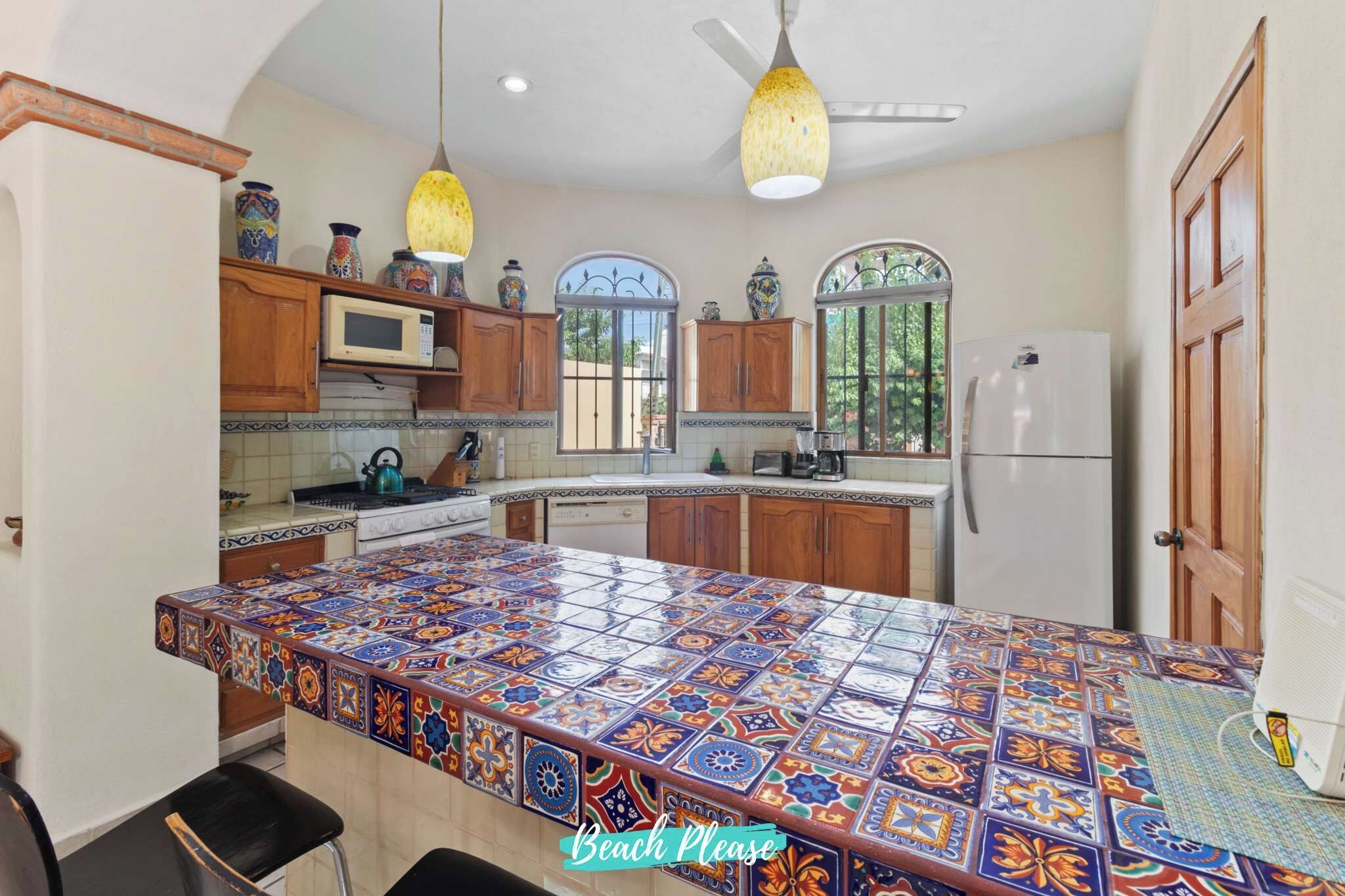 A kitchen with a colorful tiled island, wooden cabinets, a microwave, and a refrigerator.