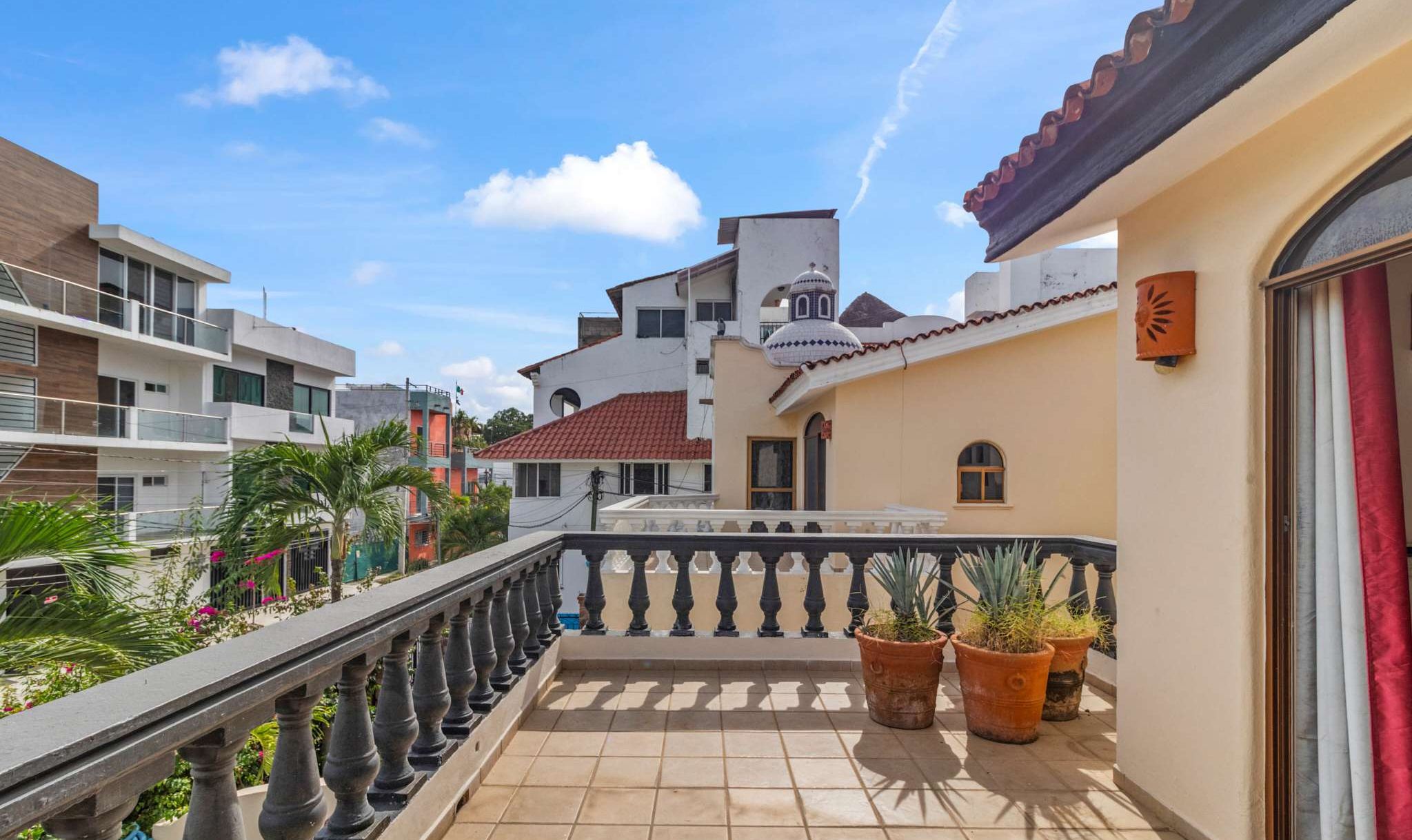 A residential balcony with a tiled floor, potted plants, and a view of neighboring buildings.