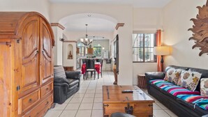 A spacious living room with a large wooden cabinet, a black leather sofa with colorful cushions, a wooden coffee table, and a kitchen in the background. - Casa Sandy - Private Golden Zone Villa with Pool (Bucerías)