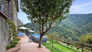 Una terraza con piscina, mobiliario exterior y vistas a una montaña boscosa.