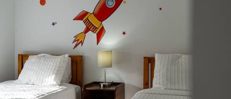 A hotel room with two beds, a nightstand with a lamp, and a wall mural of a rocket.