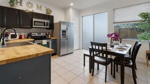 A modern kitchen with dark cabinets, a wooden island, and a dining area with a table and chairs. - Cozy 3BDR House near Disney - AL (Kissimmee)