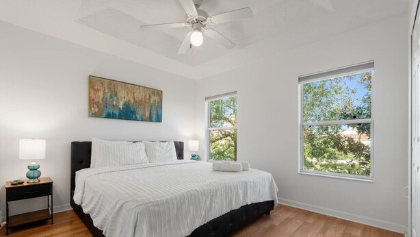 A bedroom with a bed, a ceiling fan, a painting, and two windows. - Cozy 3BDR House near Disney - AL (Kissimmee)