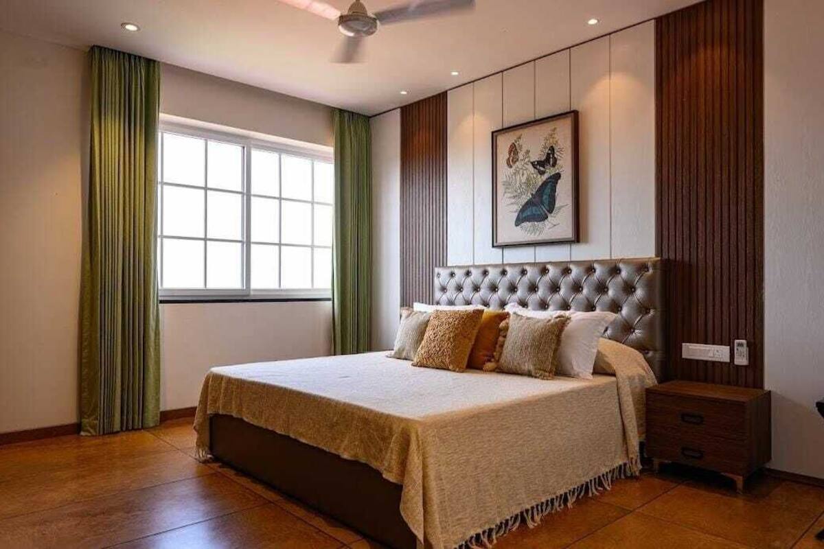 Une chambre avec un grand lit, un ventilateur de plafond, une fenêtre avec des rideaux et une œuvre d’art encadrée accrochée au mur.