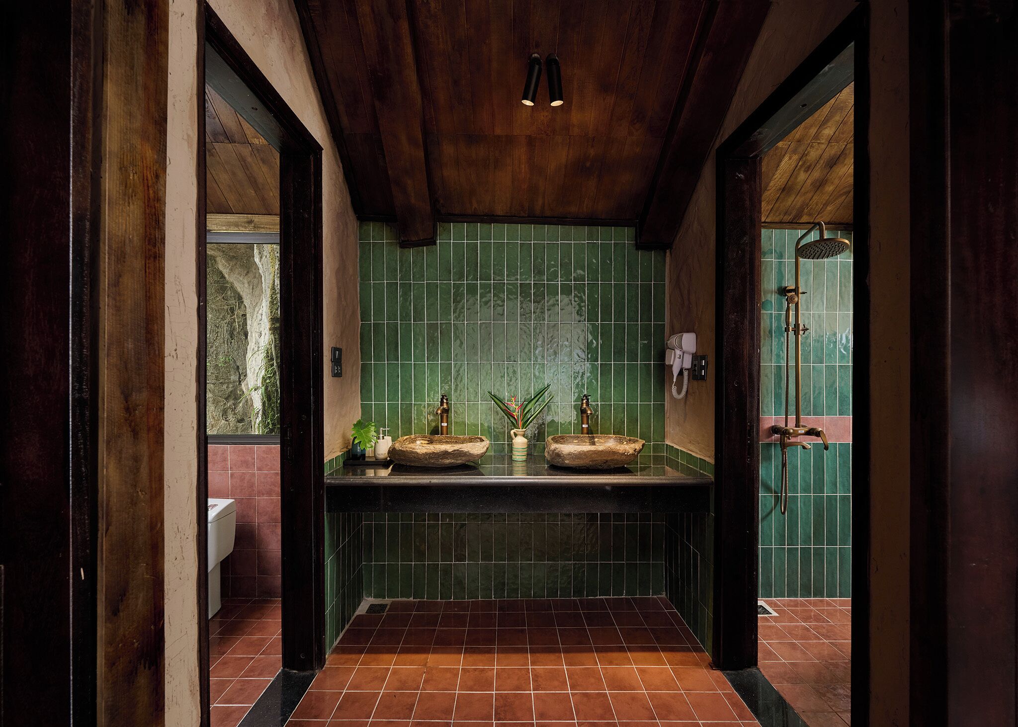 Une salle de bain avec un mur recouvert de carreaux verts, deux lavabos, une douche et un plafond en bois.