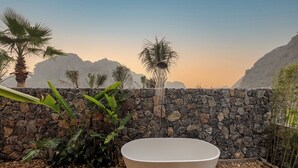 A spa area with a stone wall, a large white bathtub, and tropical plants. - Chay Mountain Retreat Ninh Binh (Hoa Lu)