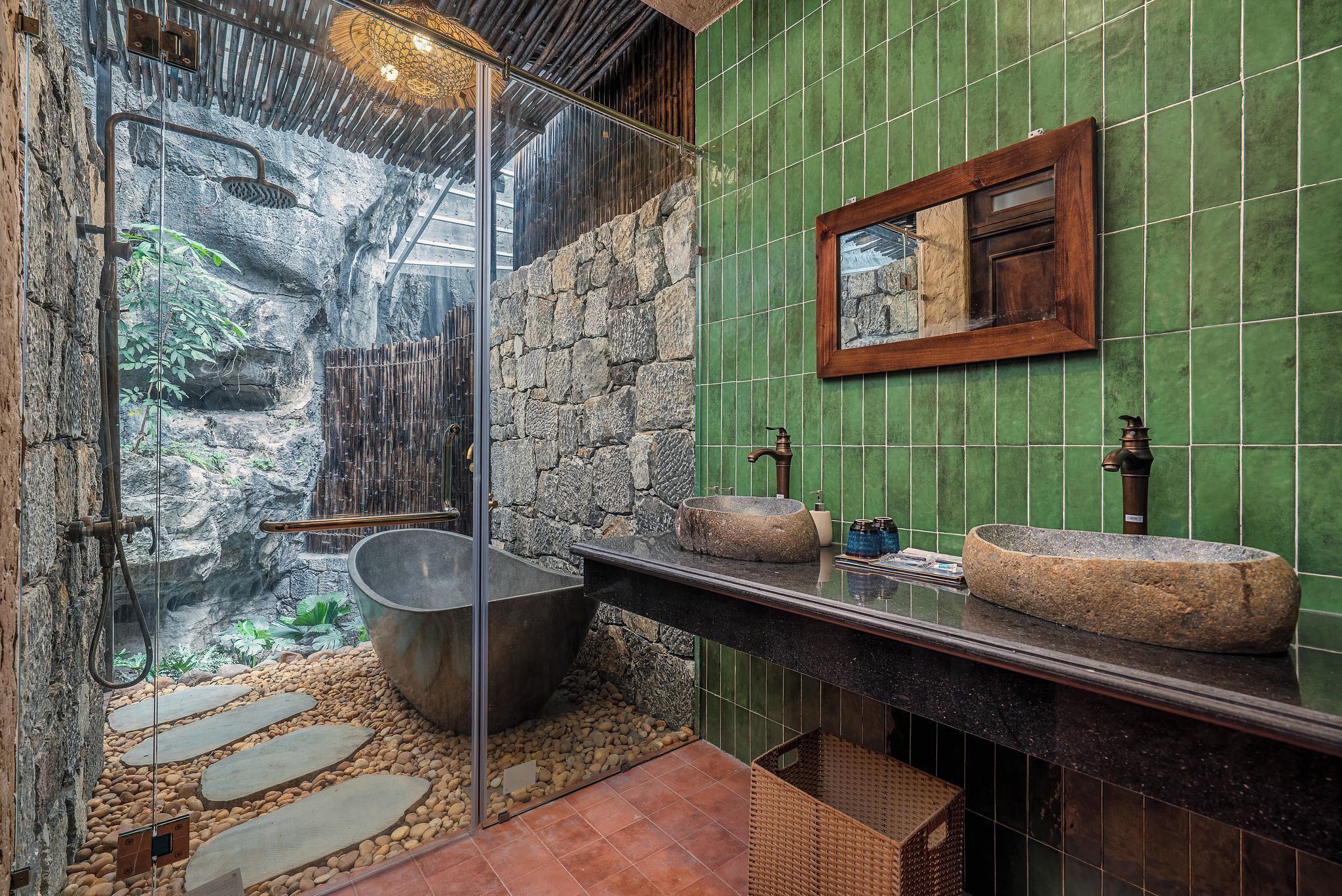 A bathroom with a stone sink, a large bathtub, and a glass-enclosed shower area with a rocky backdrop.
