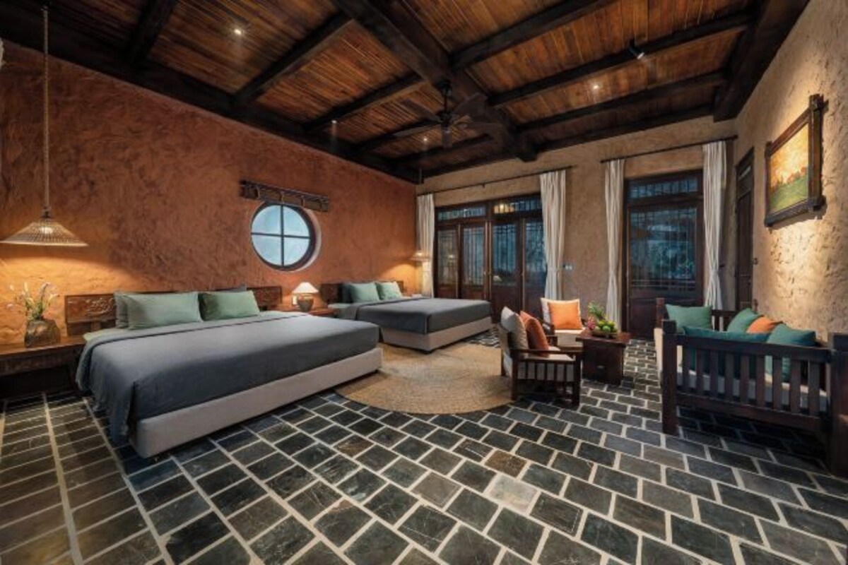 Una habitación con una cama grande, un sofá, un banco de madera y un ventanal redondo.