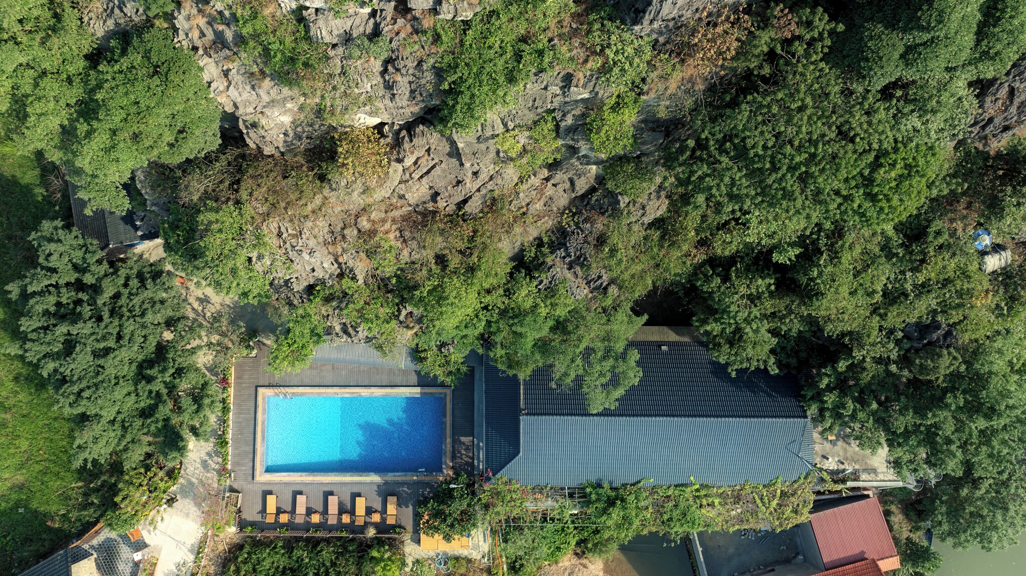 An aerial view of a property with a swimming pool, lounge chairs, and a rocky cliff.