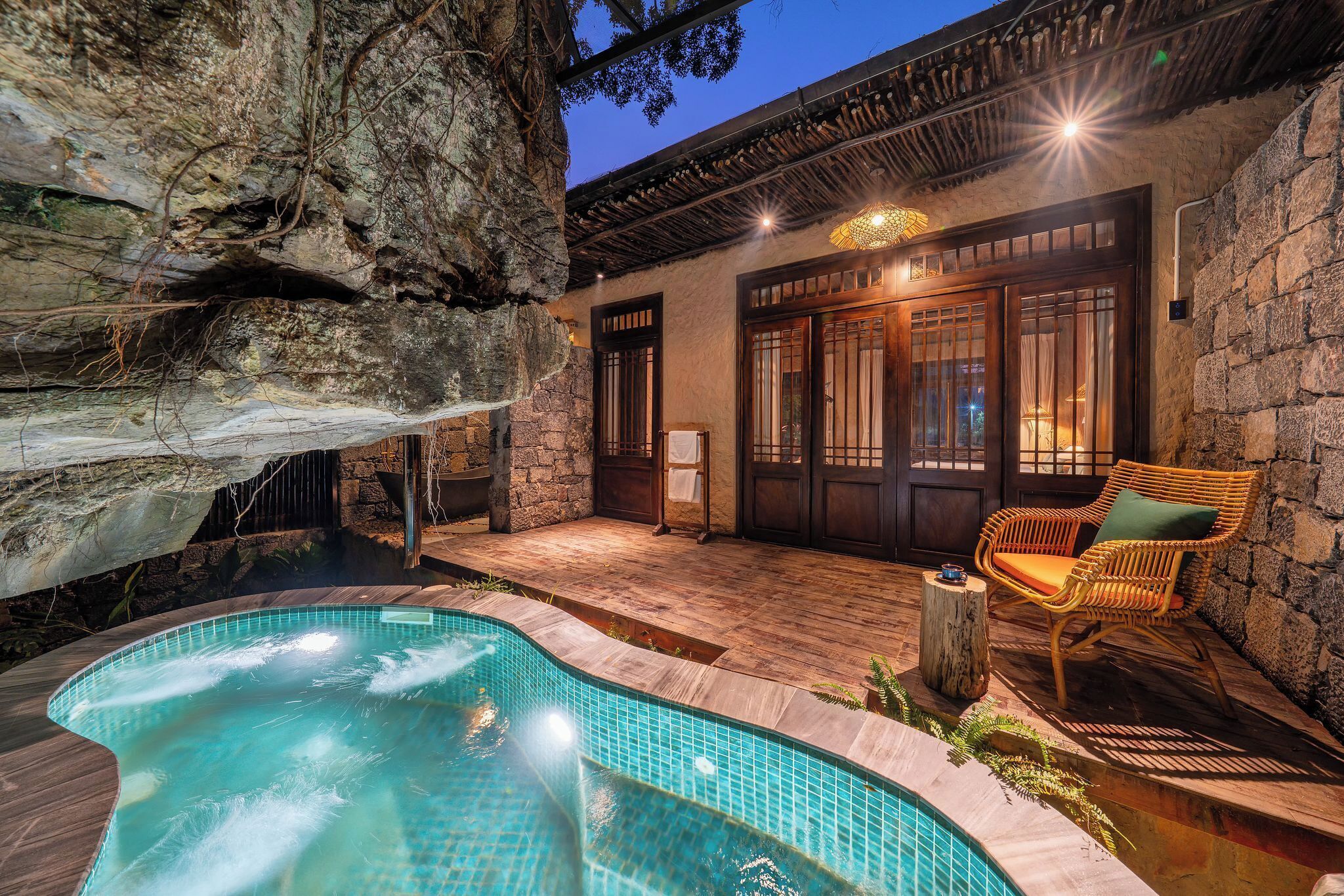 A pool area with a stone wall, wooden deck, and a wicker chair.