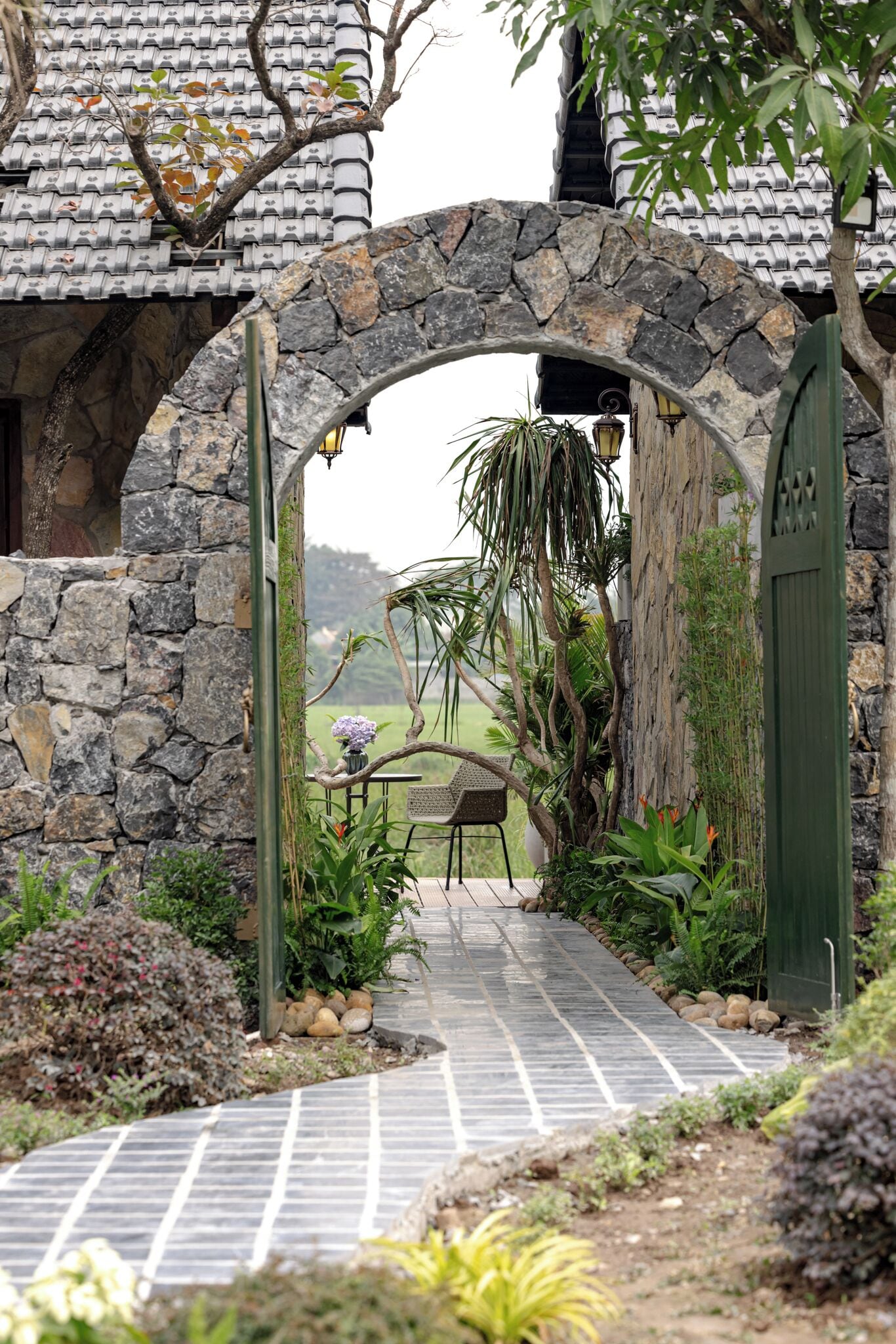A stone archway leading to a pathway with a view of a traditional house and a garden.