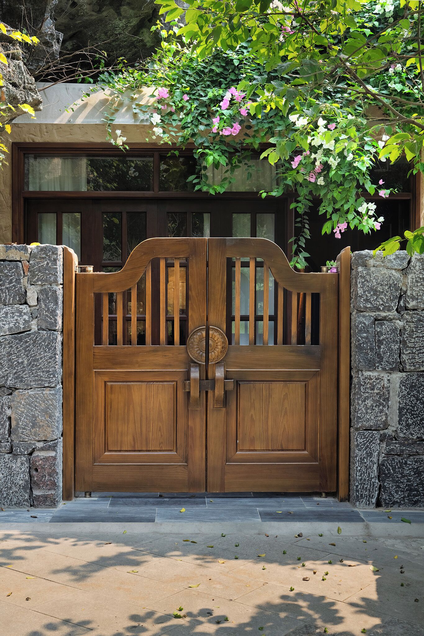 A wooden gate with a keyhole, flanked by stone walls, leading to a building with windows.