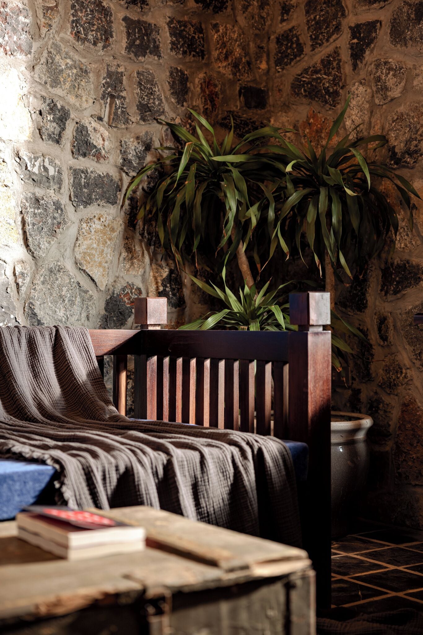 A cozy room with a stone wall, a wooden chair, a potted plant, and a blanket on the chair.