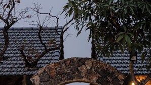 A stone archway leading to a building with a tiled roof, surrounded by plants and a pathway. - Chay Mountain Retreat Ninh Binh (Hoa Lu)