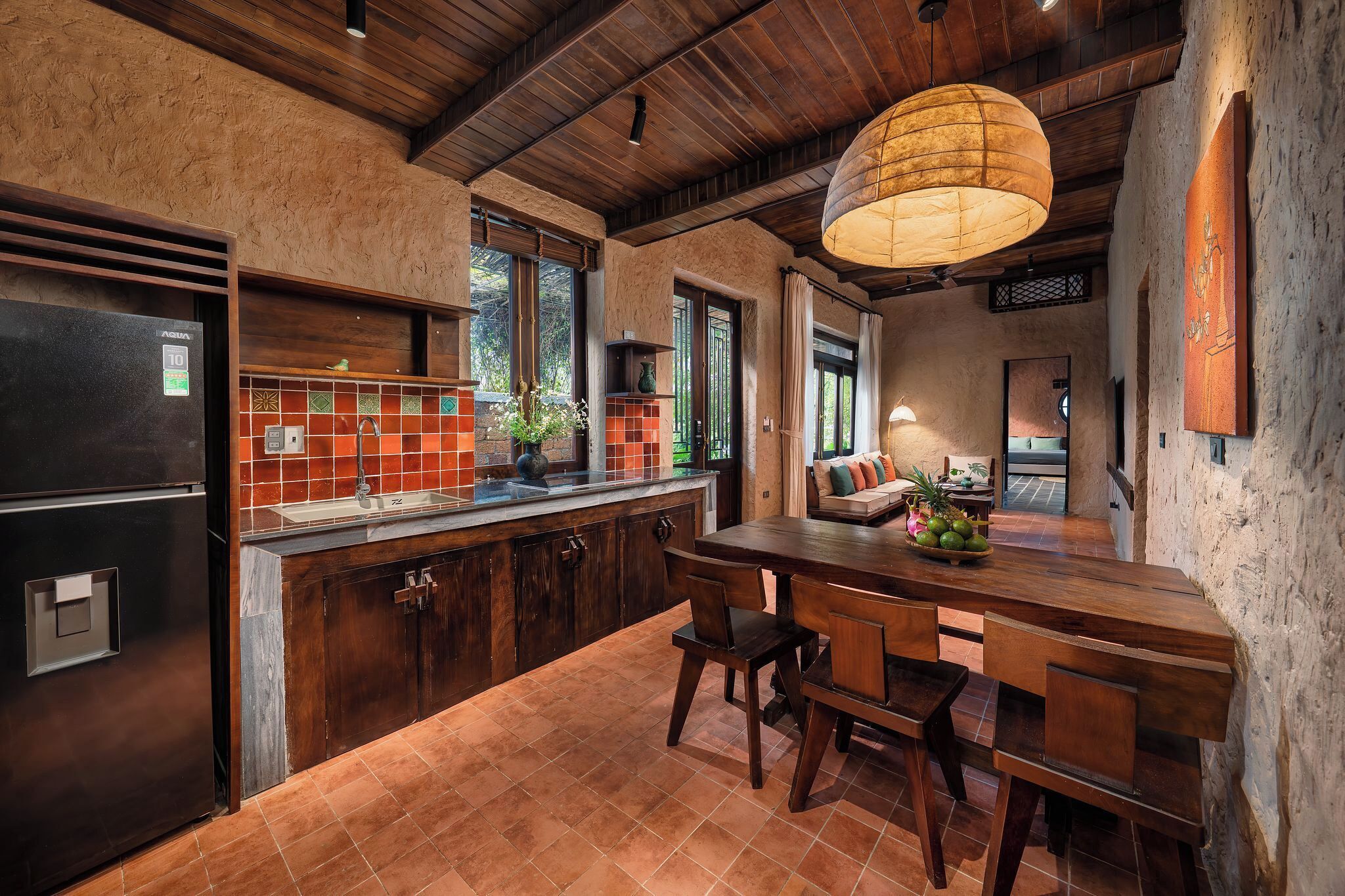 A kitchen with a wooden ceiling, a large island with chairs, and a hanging light fixture.