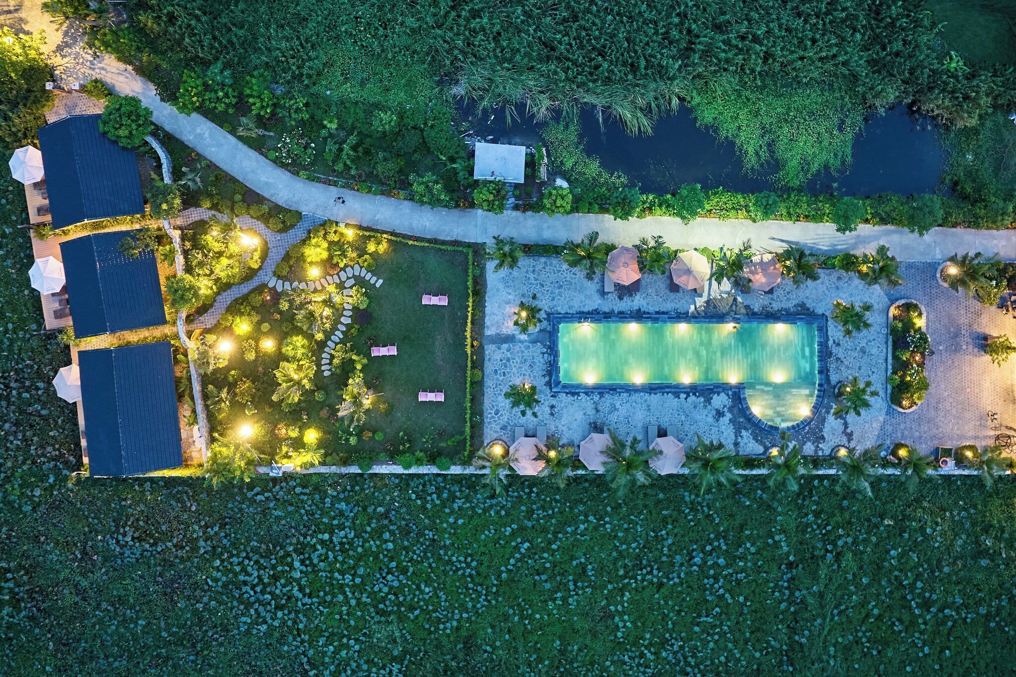 An aerial view of a resort with a swimming pool, lounge areas, and a well-maintained garden.
