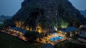 A resort with a swimming pool, wooden cabins, and a large mountain backdrop. - Chay Mountain Retreat Ninh Binh (Hoa Lu)
