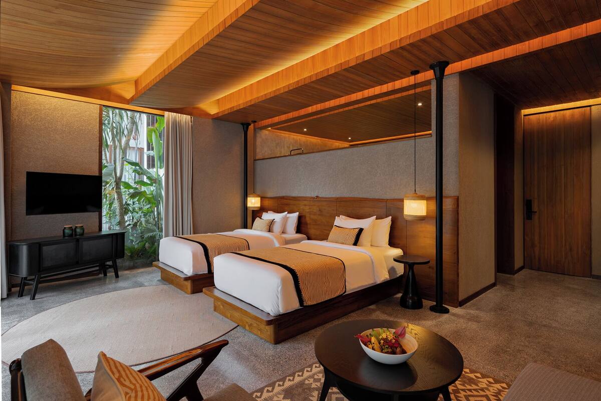 A modern hotel room with a large bed, a TV, a desk, and a view of greenery.