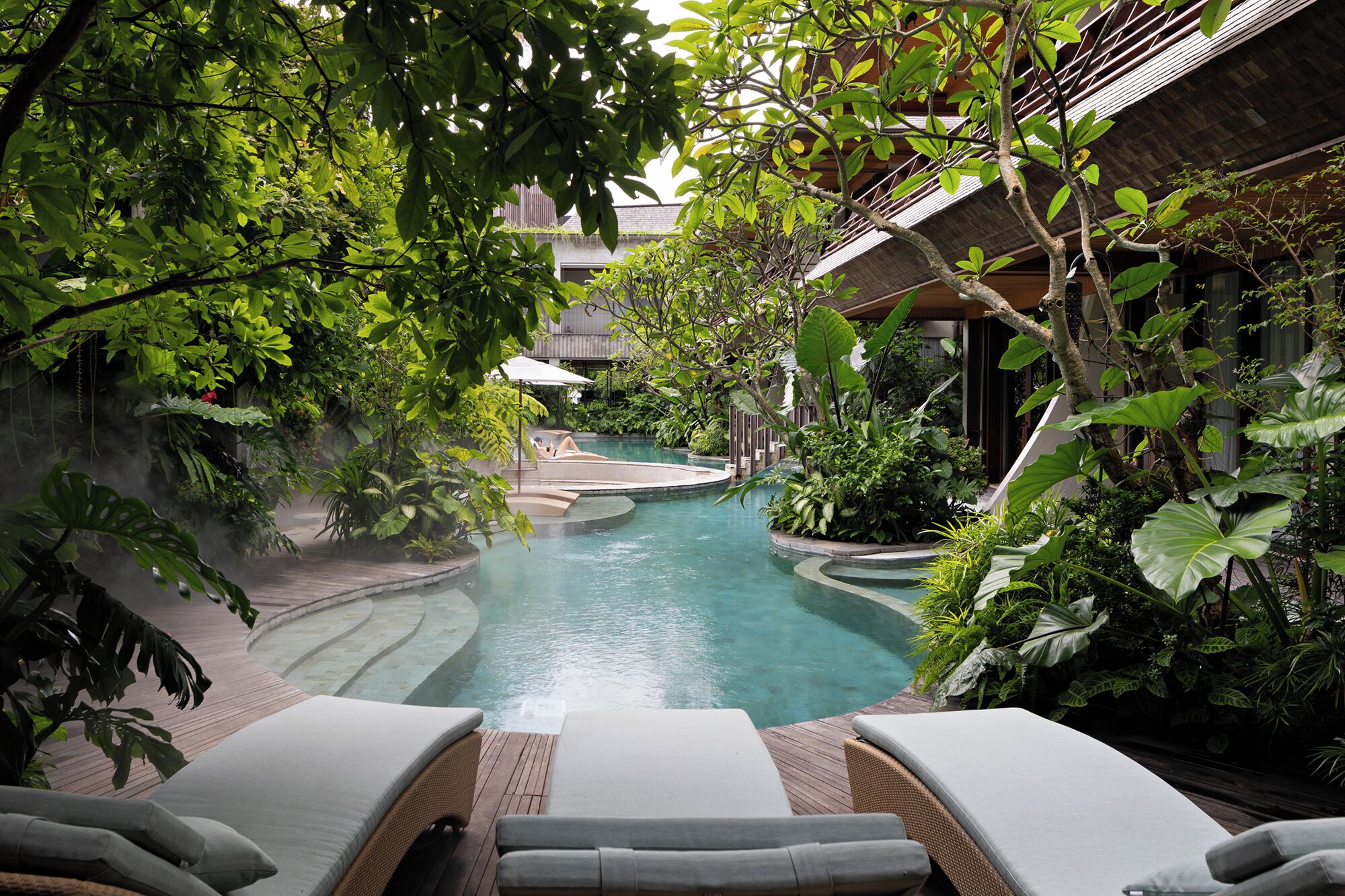 Un área de piscina interior tranquila, rodeada de abundante vegetación, con sillones de descanso y una piscina pequeña.
