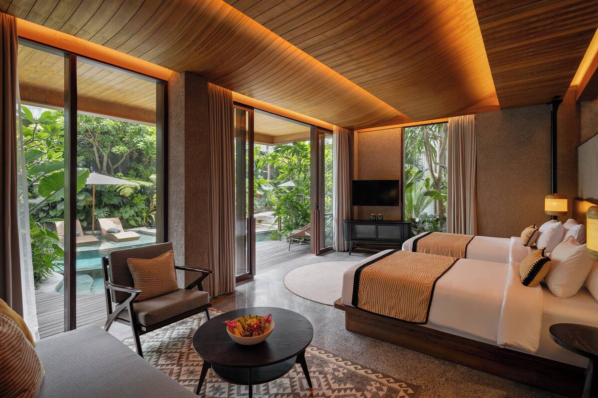 A modern hotel room with a large bed, a TV, and a view of a pool and greenery.
