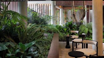 An indoor garden with seating areas, including chairs and tables, surrounded by lush greenery and bamboo plants.
