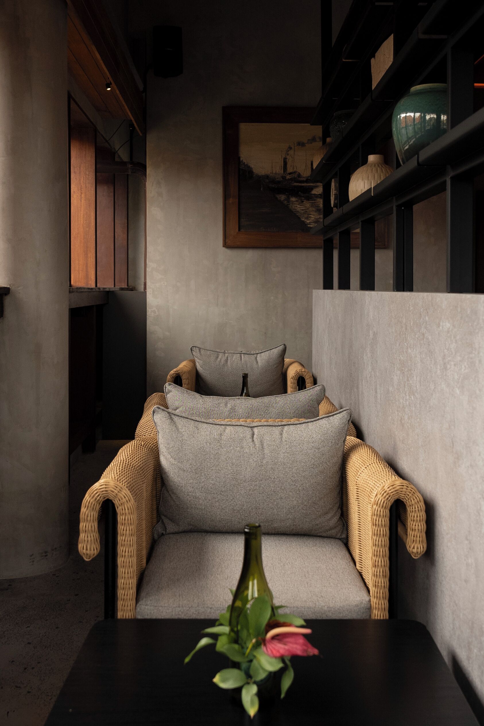 A modern interior with a grey sofa, wicker armchairs, a black table, and a vase with flowers.