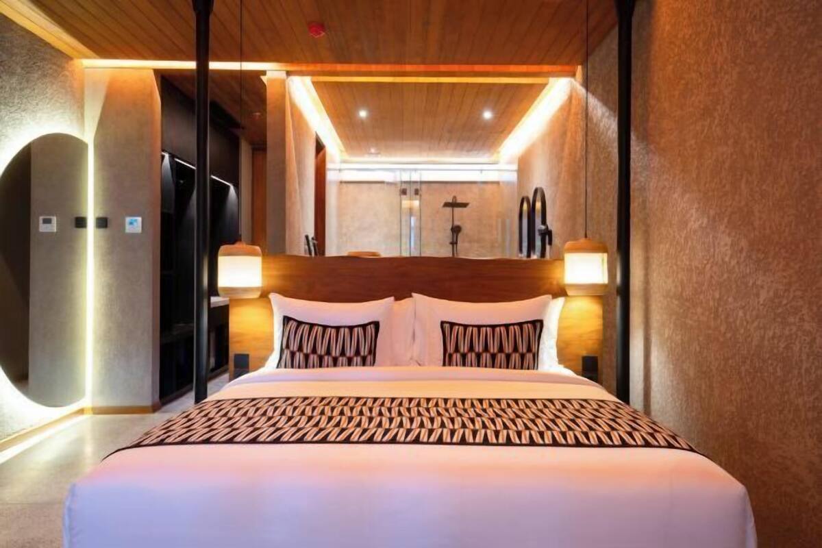 A modern hotel room with a large bed, two bedside lamps, and a wooden ceiling.
