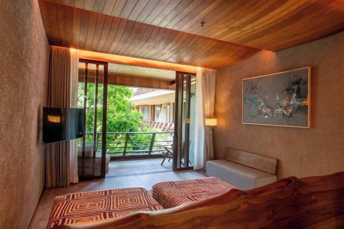 A room with a bed, a TV, a painting, and a view of greenery outside.