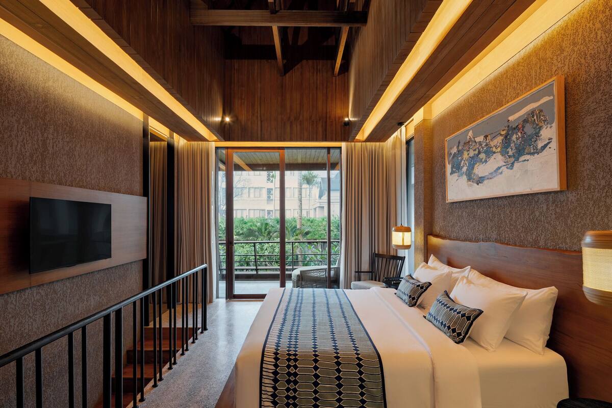 A hotel room with a bed, a TV, a painting, and a balcony with a view.