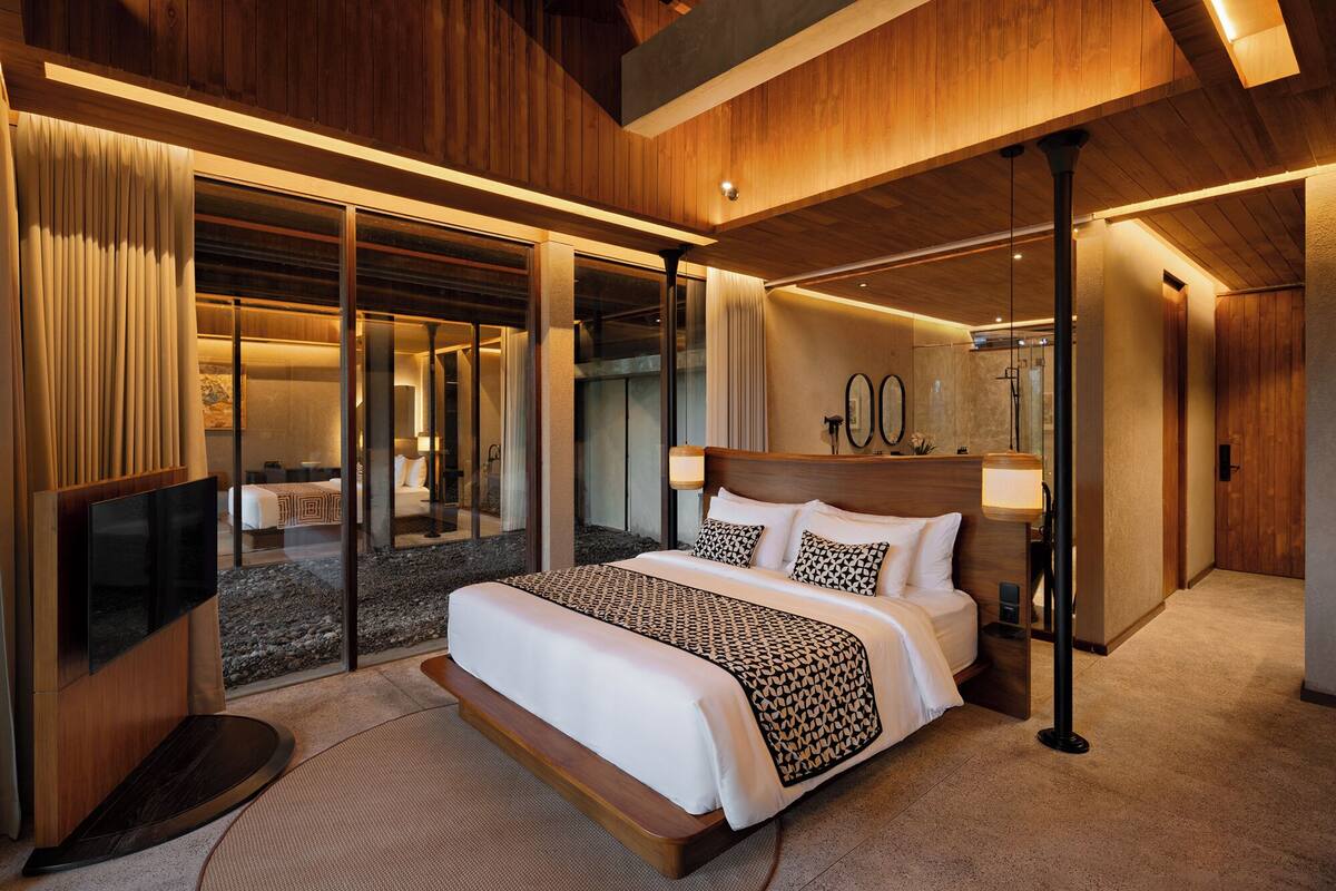 A modern hotel room with a large bed, a television, and a sliding glass door leading to a balcony.