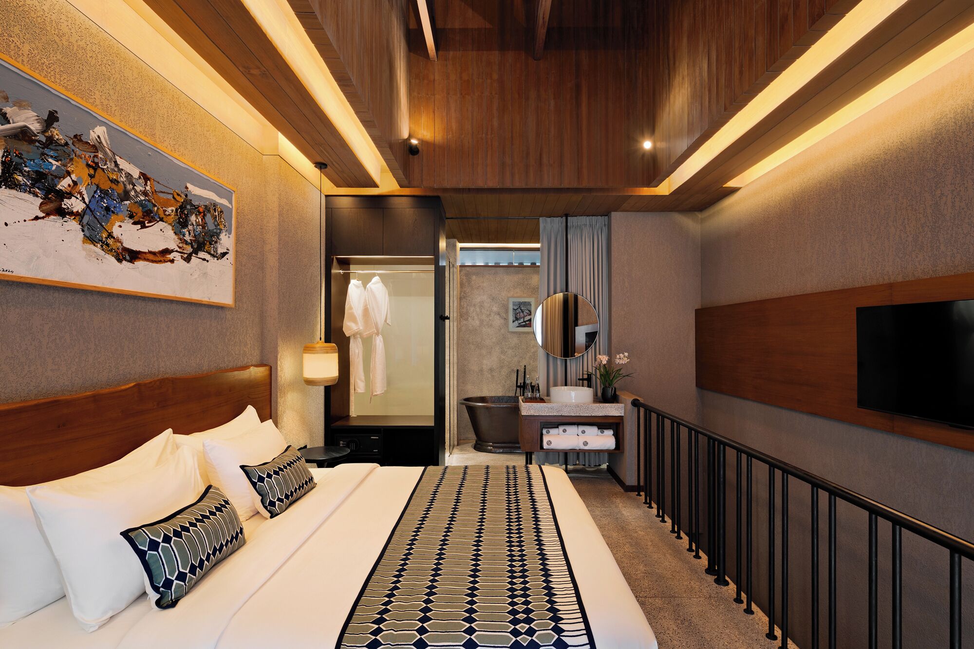 Een moderne hotelkamer met een groot bed, een badkamer met badkuip, een wastafel met spiegel en een aan de muur bevestigde televisie.