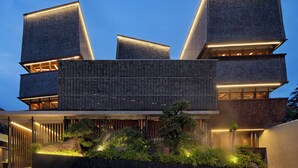 A modern building with multiple levels and illuminated edges, featuring a landscaped garden area with various plants. - The Kemilau Ubud (Ubud)