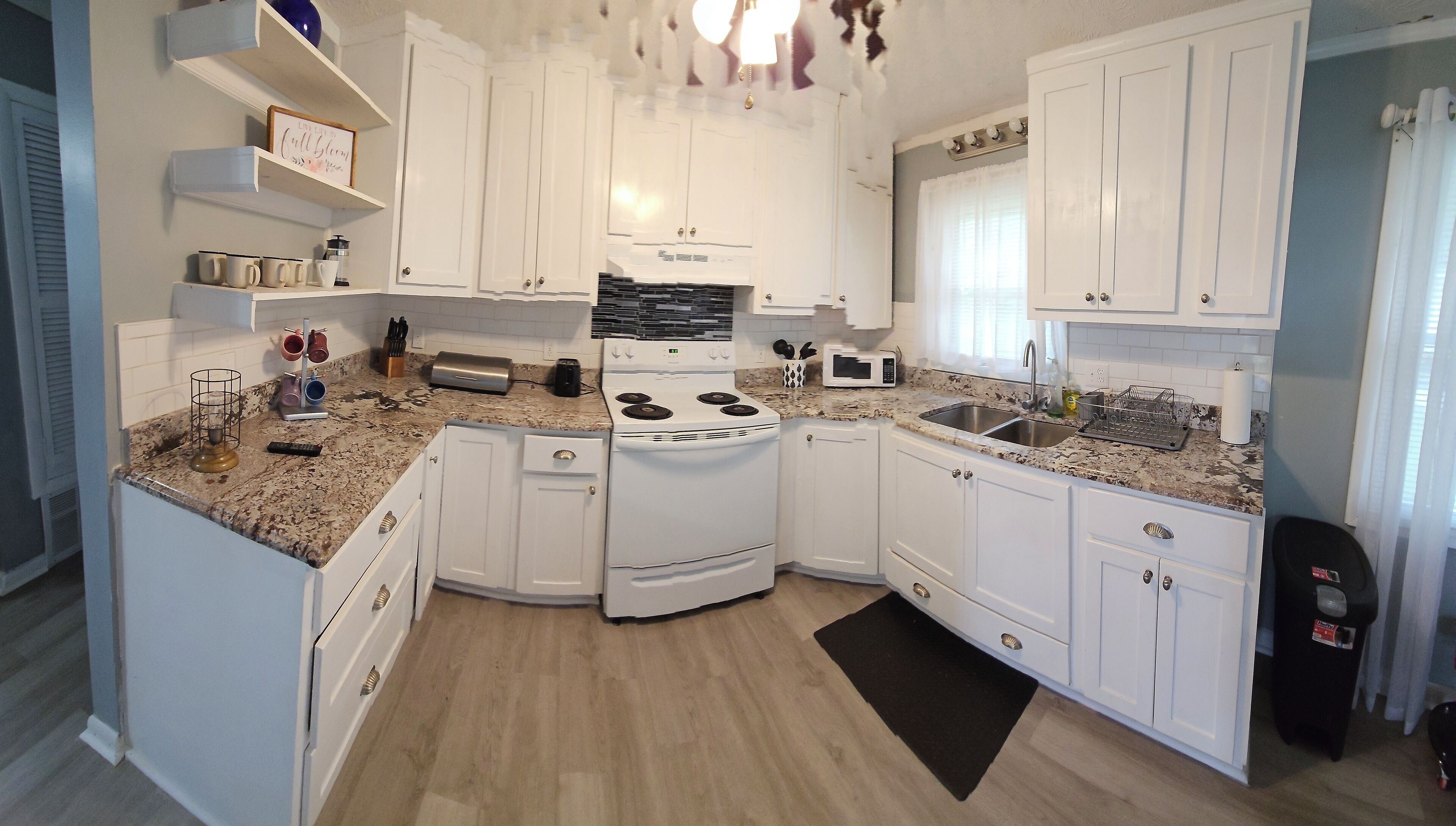 A compact kitchen with white cabinets, a stove, a microwave, and a sink.