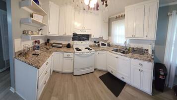 A compact kitchen with white cabinets, a stove, a microwave, and a sink.