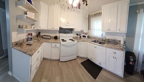 A compact kitchen with white cabinets, a stove, a microwave, and a sink.
