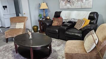 A living room with a black leather sofa, two armchairs, a coffee table, and a painting on the wall.