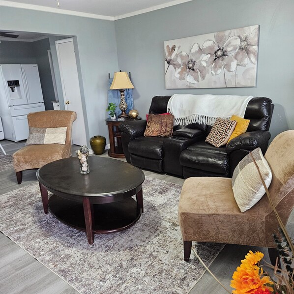 A living room with a black leather sofa, two armchairs, a coffee table, and a painting on the wall.