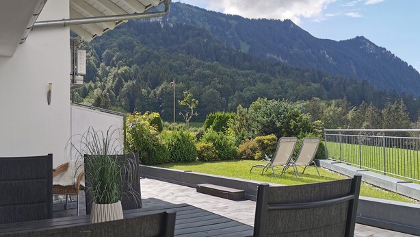 Een balkon met buitenmeubilair, een potplant en uitzicht op een berg.