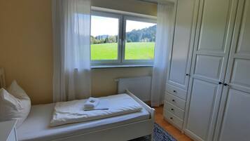 Un dormitorio con cama, ventana que da a un campo verde, radiador y armario.