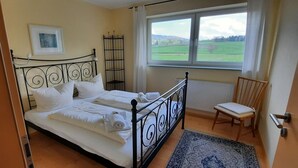 Een slaapkamer met een bed, een stoel, een raam met uitzicht en een radiator.