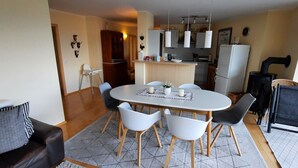 Een eetgedeelte met een ronde tafel, zes stoelen, een keuken op de achtergrond en een raam met uitzicht.