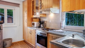 A kitchen with wooden cabinets, a microwave, a stove, and a sink. - Holiday Home 'Alpen Lodge' with Mountain View, Private Terrace and Wi-Fi (Garmisch-Partenkirchen)