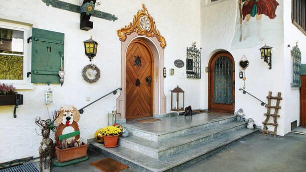 A building with a wooden door, steps, a dog sculpture, and a lantern. - Holiday Home 'Alpen Lodge' with Mountain View, Private Terrace and Wi-Fi (Garmisch-Partenkirchen)