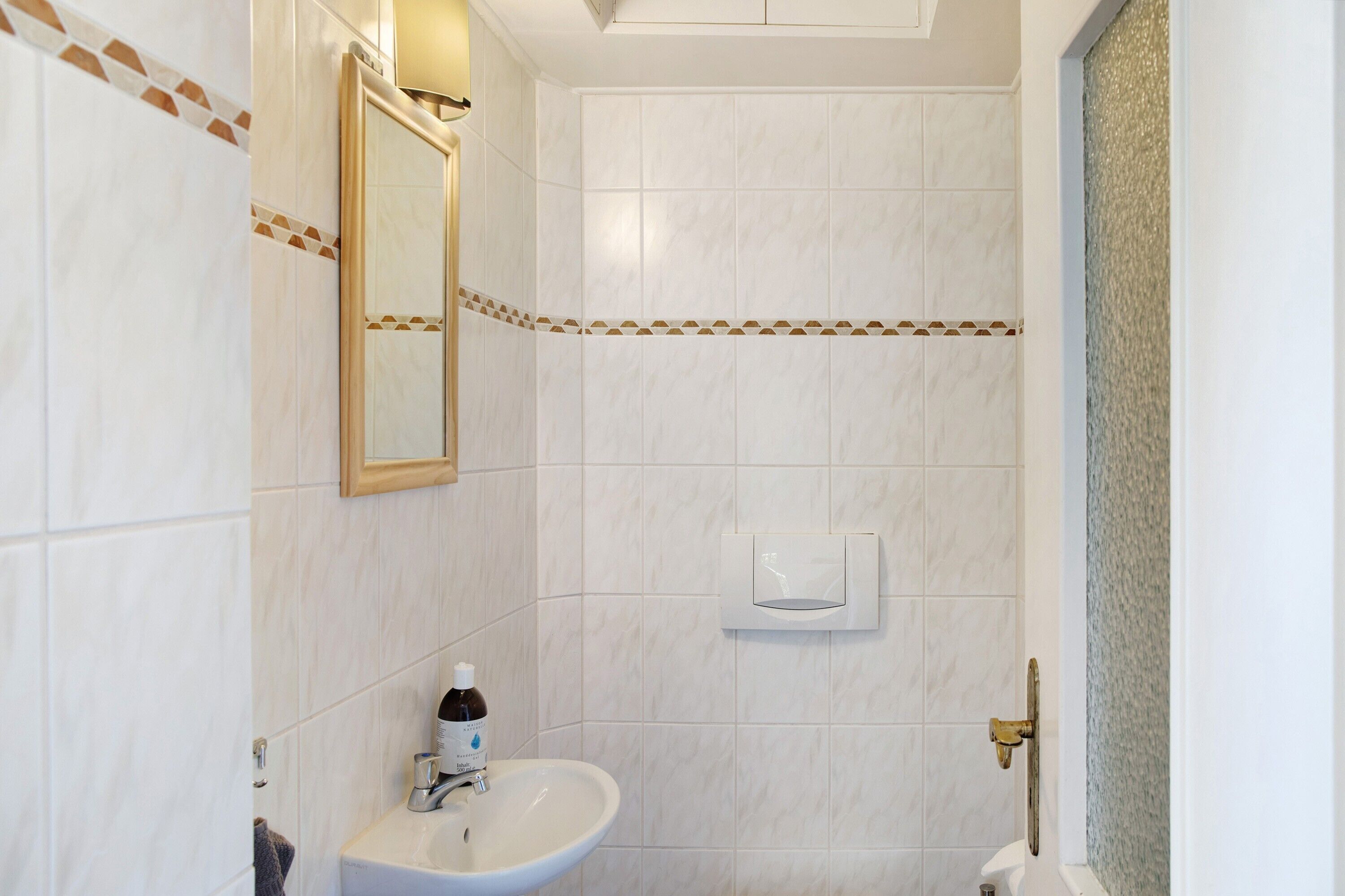 A bathroom with white tiles, a mirror, a sink, a soap dispenser, and a towel rack.